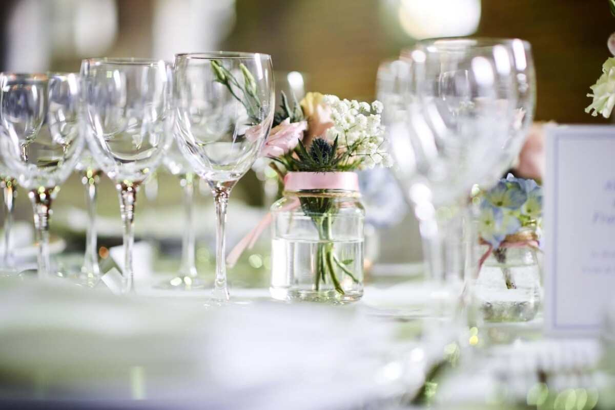 domaine-de-mehaignoul118 Verres à pied alignés sur une table avec un vase en verre contenant des fleurs, décoré pour un événement.