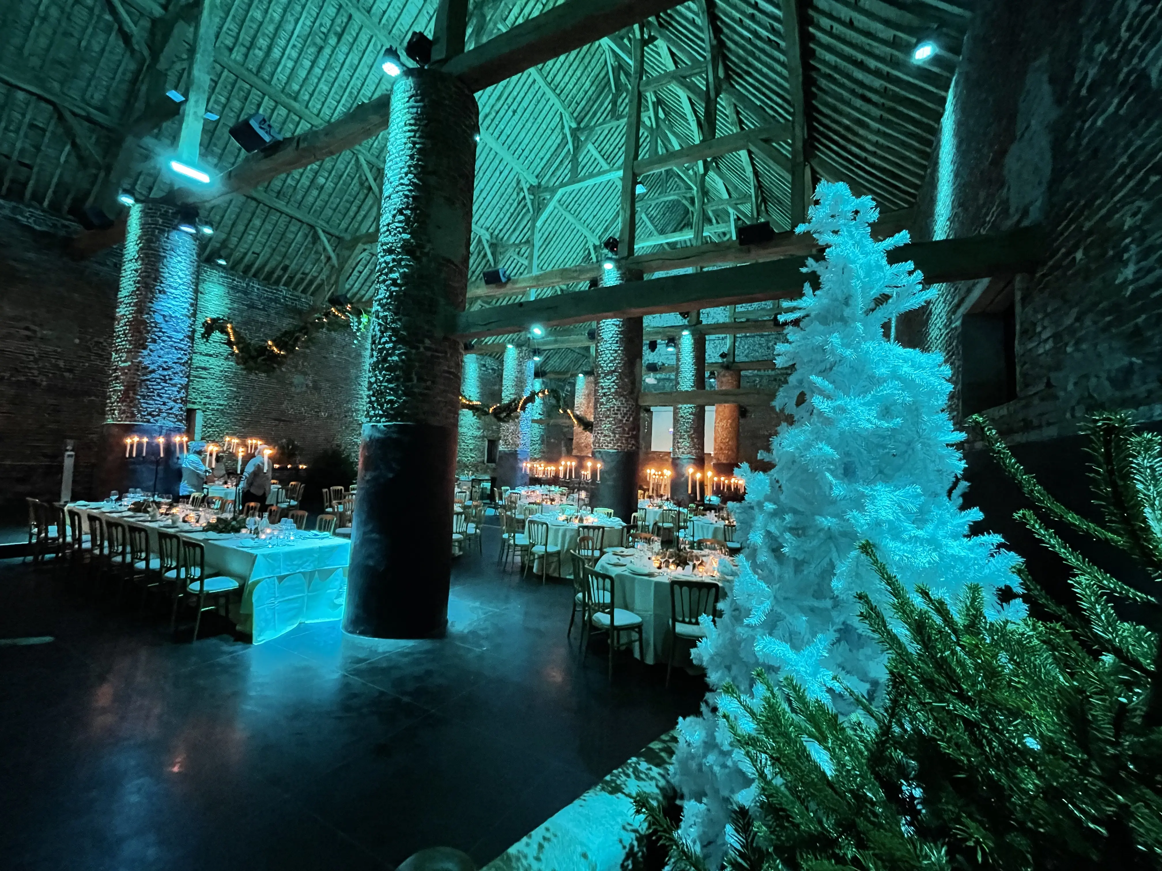 evenement-traiteur-mariage-mehaignoul129 Salle de réception avec tables décorées, chandeliers allumés, colonnes en pierre et arbre blanc sous éclairage bleuté au Domaine de Mehaignoul.