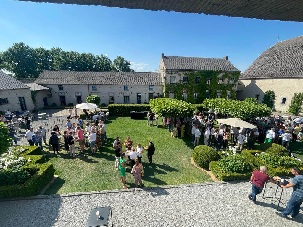 domaine-de-mehaignoul9 Groupes de personnes rassemblés dans une cour verdoyante du Domaine de Mehaignoul, entourés de bâtiments en pierre et de haies taillées.