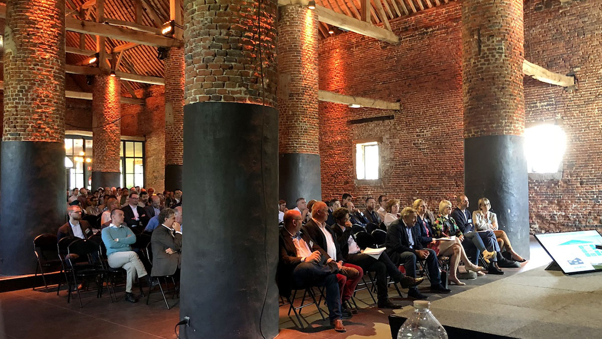seminaire-salle Des participants assis dans une salle en briques avec de grandes colonnes, écoutant une présentation au Domaine de Mehaignoul.
